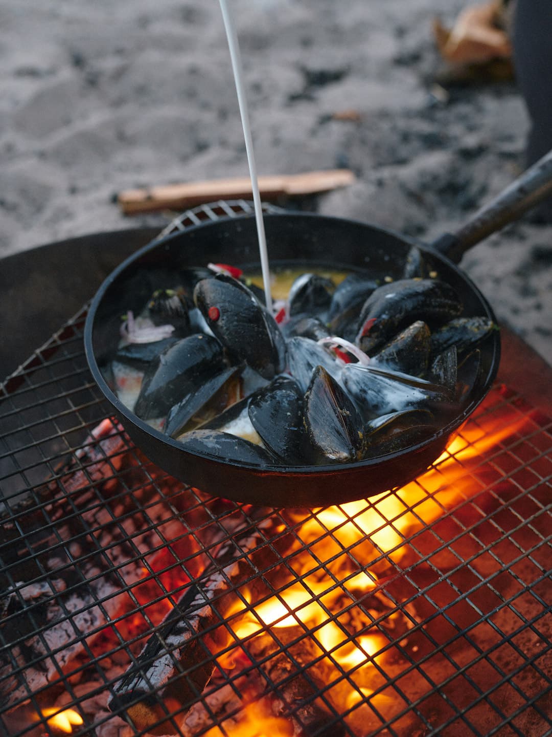 Mussels being cooked in a pan on a fireplace