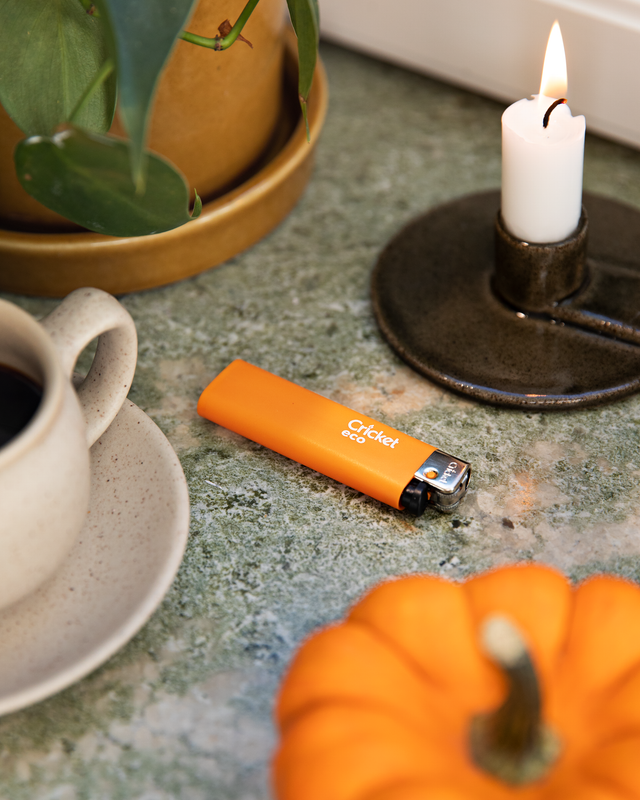 Orange lighter lying on a marble table with candle and coffee mug